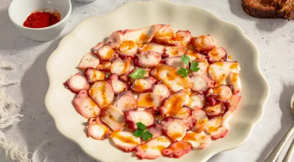 Delicioso carpaccio de pulpo con pimentón y perejil, servido en plato blanco. Acompañado de pan tostado y especias.