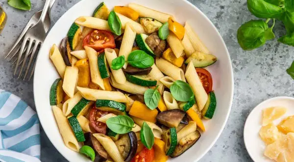 Macarrones con verduras asadas: calabacín, berenjena, pimientos y tomates, decorados con albahaca fresca. ¡Una forma deliciosa de aprender como hacer macarrones!
