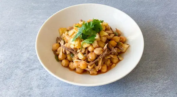 Un plato de ropa vieja canaria, con garbanzos, carne deshebrada y patatas fritas, adornado con perejil fresco.