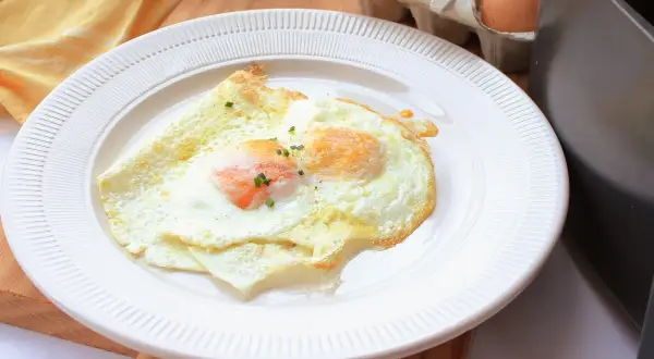 Dos huevos fritos perfectos, cocinados en freidora de aire, servidos en un plato blanco. Un toque de cebollino fresco adorna las yemas.