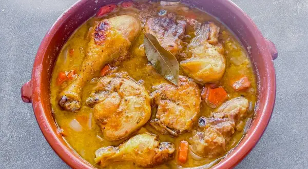 Muslos de pollo en salsa, un plato casero que evoca la receta de la abuela, con trozos de zanahoria y laurel.