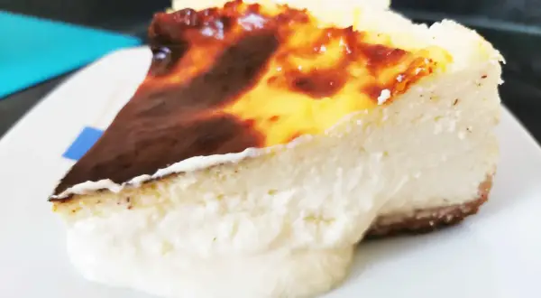 Porción cremosa de tarta de queso con la parte superior dorada y caramelizada, lista para ser disfrutada.