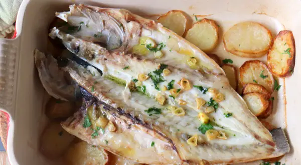Lubina a la espalda horneada con patatas, ajo y perejil en una bandeja.