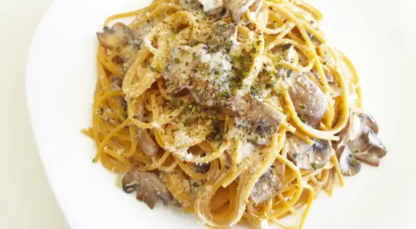 Espaguetis con nata y champiñones, cubiertos con queso rallado y hierbas aromáticas. Un plato cremoso y delicioso.