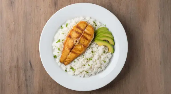Un delicioso plato de arroz con pescado a la parrilla, acompañado de aguacate en rodajas y perejil picado.