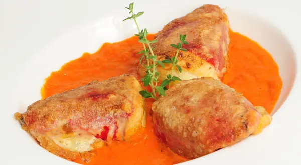 Pimientos rellenos de bacalao, dorados y crujientes, servidos en una cremosa salsa de pimientos rojos, adornados con tomillo fresco.