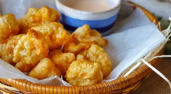 Cesta de mimbre con fritos de pixin dorados y crujientes, acompañados de una salsa rosada. ¡Un bocado delicioso!