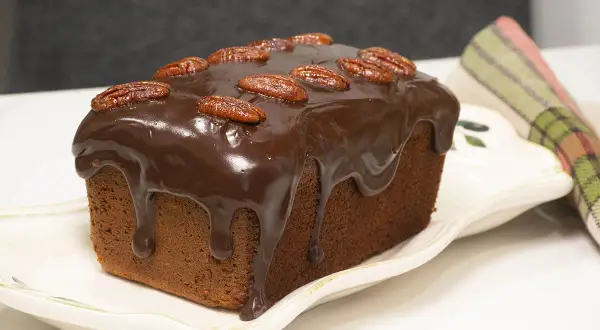 Bizcocho de plátano y chocolate cubierto de glaseado y nueces pecanas, listo para disfrutar.