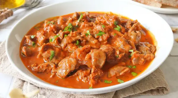 Mollejas de pollo en salsa roja, un plato casero y reconfortante, servido en un cuenco blanco con perejil picado.
