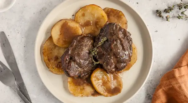 Dos jugosas galtas al horno, tiernas y cubiertas de salsa, servidas sobre rodajas de patata dorada. Un plato reconfortante.