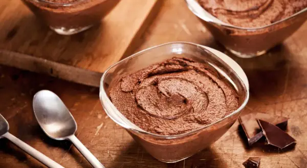 Delicioso mousse de chocolate en copas de cristal, listo para disfrutar. Trozos de chocolate negro al lado.