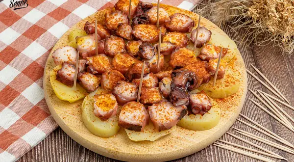 Pulpo a la gallega servido sobre patatas cocidas, espolvoreado con pimentón y servido con palillos.