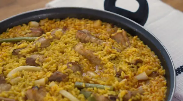 Paella recién hecha, un plato perfecto para tus recetas de arroz. Con trozos de carne, judías verdes y un arroz amarillo vibrante.