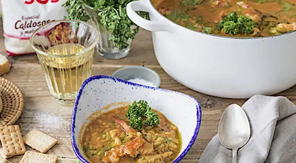 Un delicioso arroz con bogavante, servido en un cuenco con perejil fresco. A su lado, galletas saladas y una copa de vino blanco.