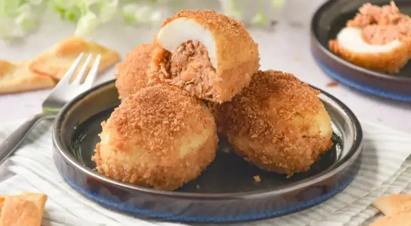 Deliciosos huevos rellenos rebozados, crujientes por fuera y jugosos por dentro, servidos en un plato con galletas saladas.