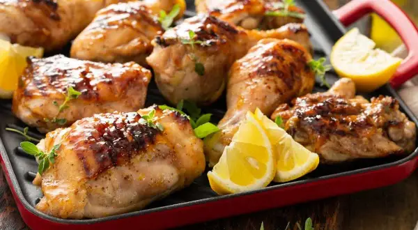 Muslos de pollo dorados y jugosos, asados a la parrilla con hierbas frescas y gajos de limón. ¡Un festín para los sentidos!