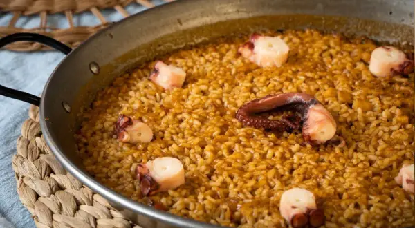 Arroz con pulpo en paellera, con trozos de pulpo bien visibles entre el arroz dorado.