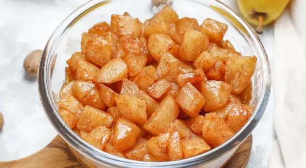 Trozos de manzana asada en freidora de aire, cubiertos de canela, en un bol de cristal.