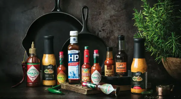 Variedad de salsas para carnes, incluyendo Tabasco, HP Sauce y Lea & Perrins, junto a chiles y romero.