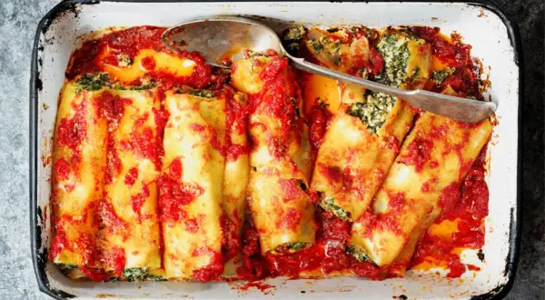 Canelones de atún horneados con salsa de tomate y espinacas, listos para servir en una bandeja.