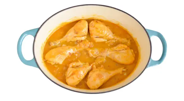 Pollo en salsa dorada, cocinándose en una olla azul. Las piezas de pollo están tiernas y cubiertas de una rica salsa.