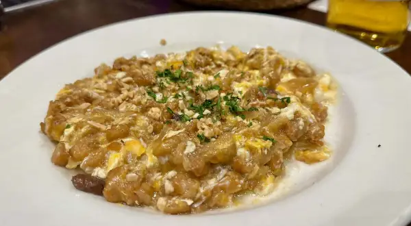 Delicioso revuelto de bacalao con trocitos de frutos secos y perejil picado, servido en plato blanco.