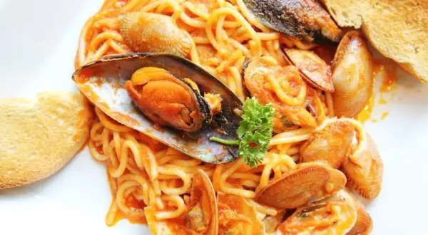 Espaguetis con almejas y mejillones en salsa roja, servidos con pan tostado. Un plato de pasta marinera delicioso.