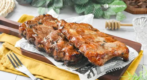 Costillas a la miel, jugosas y glaseadas, servidas sobre papel de periódico y tabla de madera.