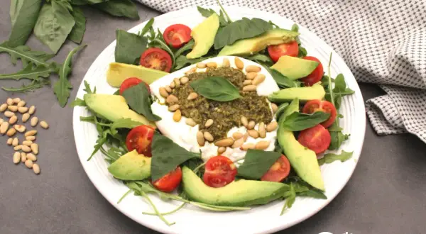 Deliciosa ensalada de burrata y pesto, con aguacate, tomates cherry y piñones.