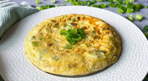 Tortilla de ajetes dorada y esponjosa, decorada con cebolleta fresca picada. Un plato sencillo y delicioso.
