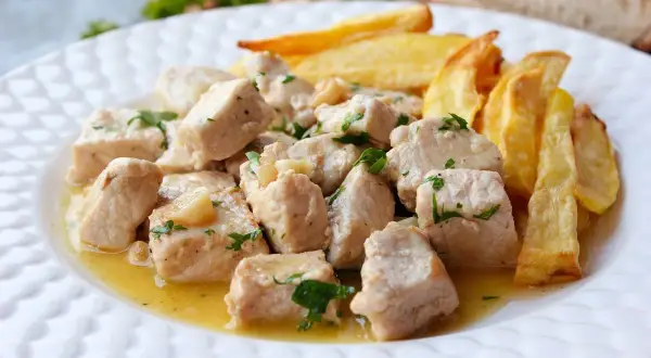 Sabroso lomo al ajillo en trozos, bañado en aceite de oliva con ajo y perejil, acompañado de patatas fritas crujientes.