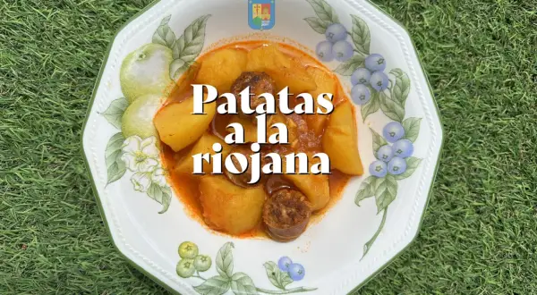 Un plato de patatas a la riojana, con trozos de chorizo y patata en una salsa rojiza, servido en una vajilla decorada con frutas y bayas.