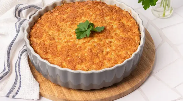 Pastel de bacalao dorado y crujiente, recién horneado en un molde gris, decorado con perejil fresco.