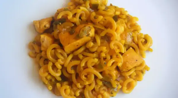 Fideuà de pollo con fideos rizados y trozos de pollo en salsa dorada, servida en plato blanco.