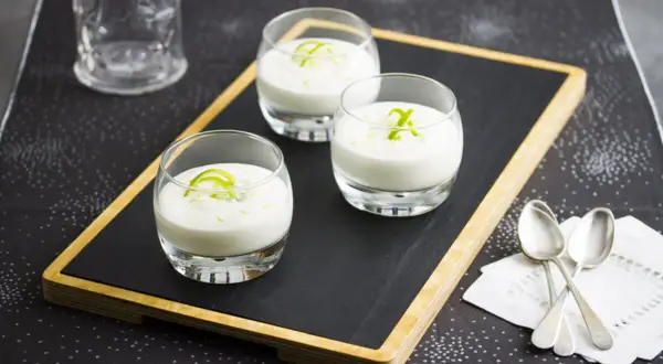 Tres vasitos de cremoso mousse de limón, decorados con ralladura verde, listos para disfrutar.