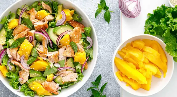 Ensalada de mango con salmón desmenuzado, aguacate, cebolla morada y hojas verdes. ¡Una explosión de sabor!
