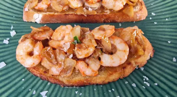 Tostadas con gambones al ajillo, cubiertas de ajo y perejil, espolvoreadas con sal marina gruesa sobre un plato verde.
