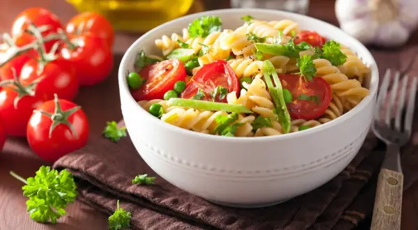 Un delicioso plato de pasta con verduras frescas, tomates cherry, guisantes y perejil.