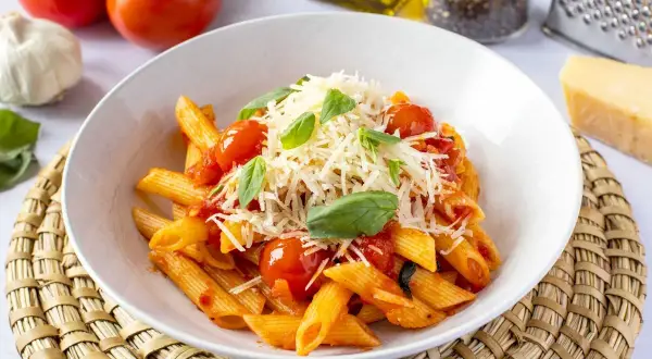 Un plato de macarrones a la napolitana con salsa de tomate, tomates cherry, albahaca fresca y queso rallado.