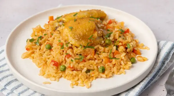 Un plato de arroz con pollo, guisantes, zanahoria y pimiento rojo, adornado con perejil picado.