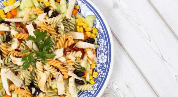 Ensalada de pasta con pollo, pepino, maíz y pasas, decorada con perejil fresco. Un plato colorido y nutritivo.
