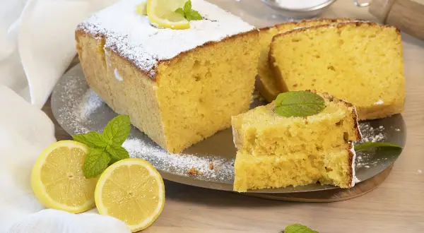 Un delicioso bizcocho de limón, espolvoreado con azúcar glas y decorado con rodajas de limón y hojas de menta.