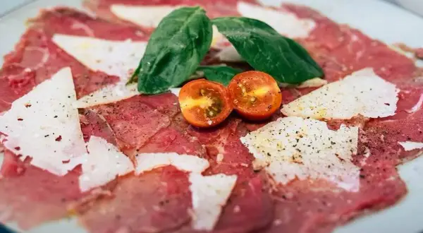 Delicado carpaccio de ternera con lascas de parmesano, hojas de albahaca y tomates cherry.