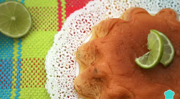 Delicioso flan de limón con rodajas de lima, servido sobre un mantel colorido y un encaje blanco.