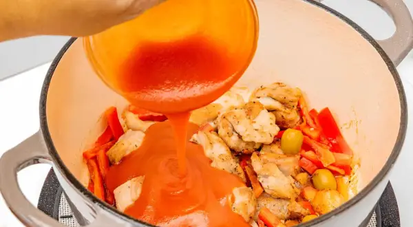 Se vierte salsa de tomate sobre trozos de pollo y pimientos en una olla.