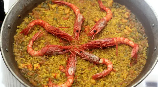Arroz con carabineros, un plato de paella con gambas rojas grandes dispuestas en círculo sobre el arroz amarillo.