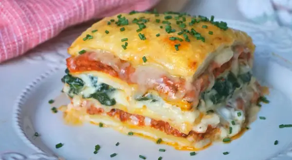 Porción de lasaña de espinacas, con capas de pasta, salsa de tomate, queso derretido y espinacas, espolvoreada con cebollín.