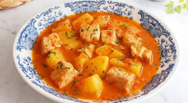 Un delicioso marmitako de atún con patatas y pimientos rojos, servido en un plato con borde azul y blanco.