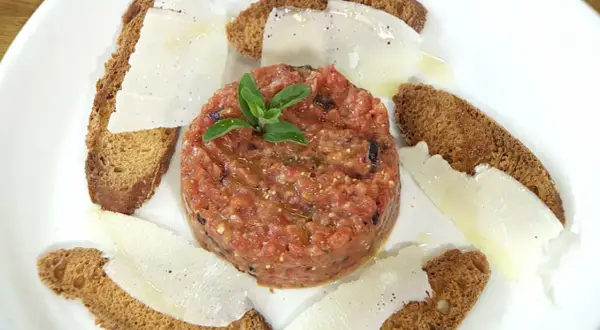 Tartar de tomate fresco, servido con finas láminas de queso y tostadas crujientes. Un bocado ligero y lleno de sabor.