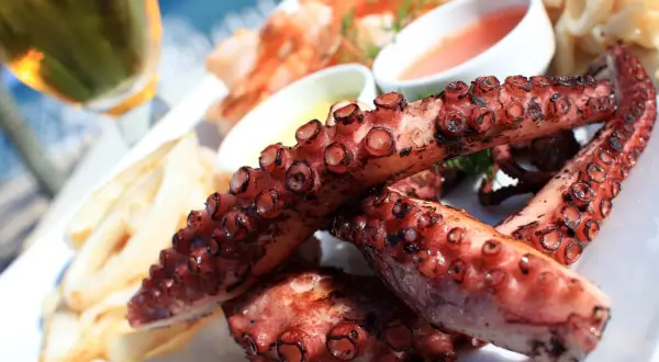 Tentáculos de pulpo a la plancha, dorados y jugosos, servidos con patatas y salsas.